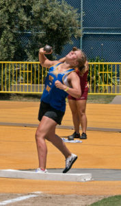 Athlete prepares for pole vault on a track with others watching.