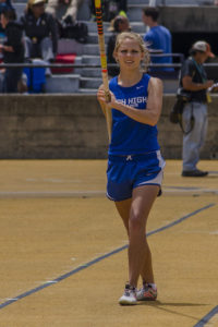 Athlete prepares for pole vault on a track with others watching.