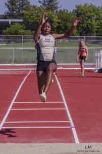 Athlete prepares for pole vault on a track with others watching.