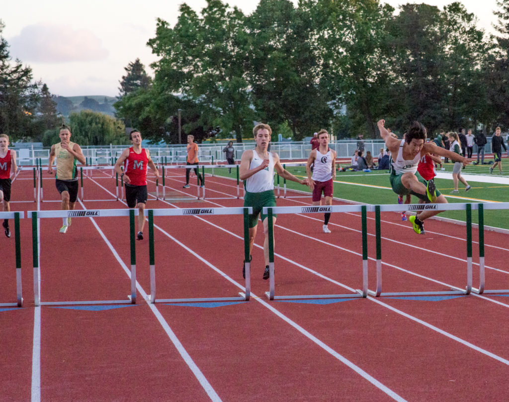 Athlete prepares for pole vault on a track with others watching.