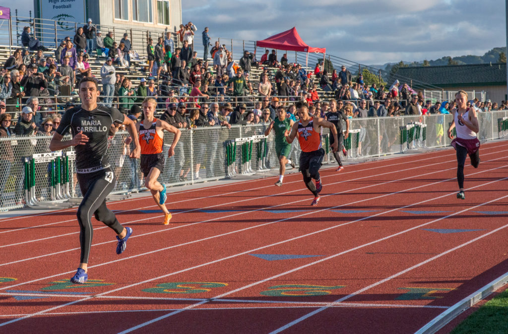 Athlete prepares for pole vault on a track with others watching.