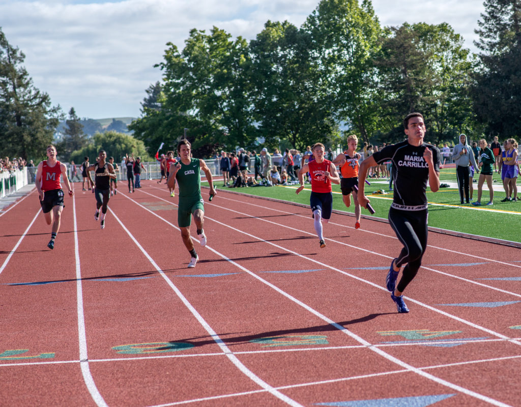 Athlete prepares for pole vault on a track with others watching.