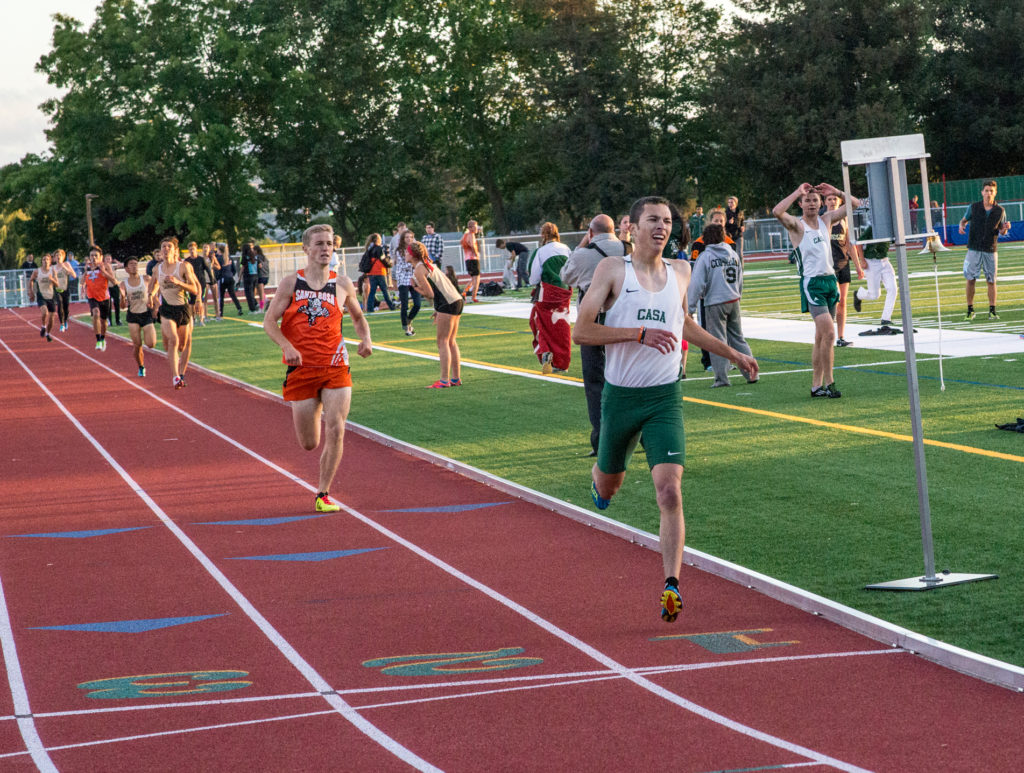 Athlete prepares for pole vault on a track with others watching.