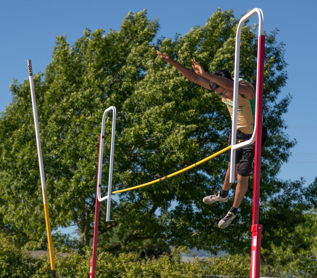 Athlete prepares for pole vault on a track with others watching.