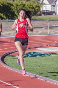 Athlete prepares for pole vault on a track with others watching.