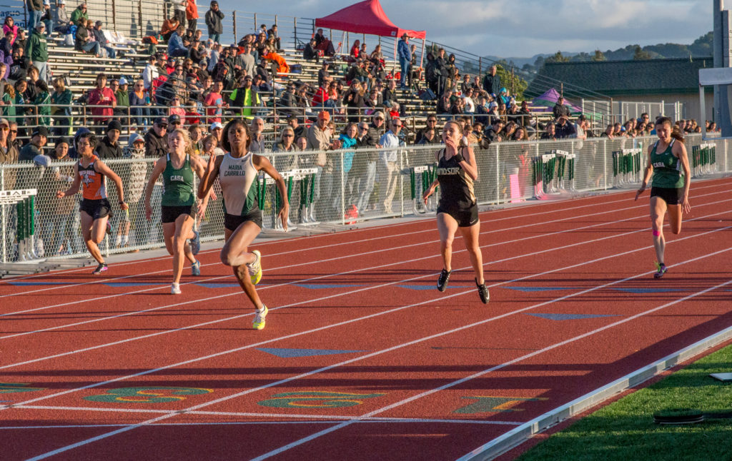 Athlete prepares for pole vault on a track with others watching.