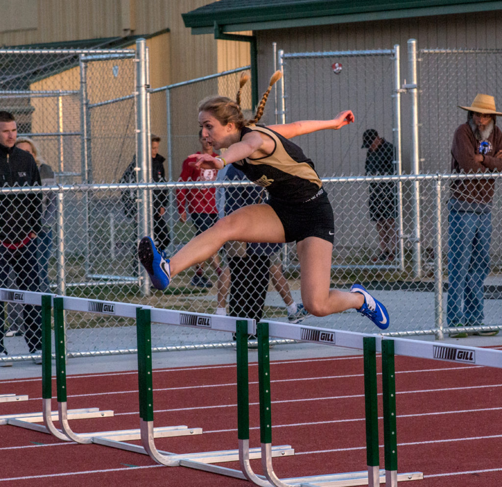 Athlete prepares for pole vault on a track with others watching.