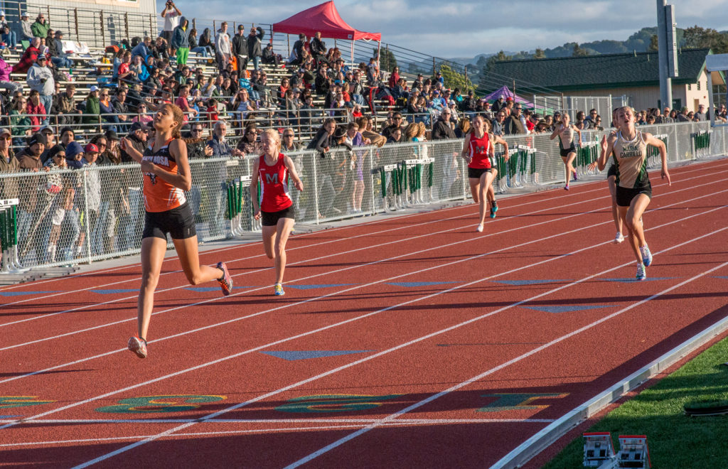 Athlete prepares for pole vault on a track with others watching.