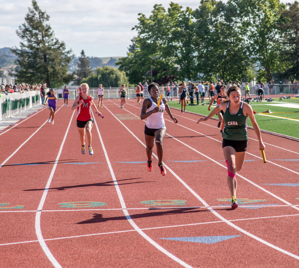 Athlete prepares for pole vault on a track with others watching.