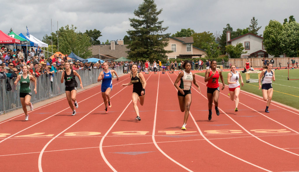 Athlete prepares for pole vault on a track with others watching.