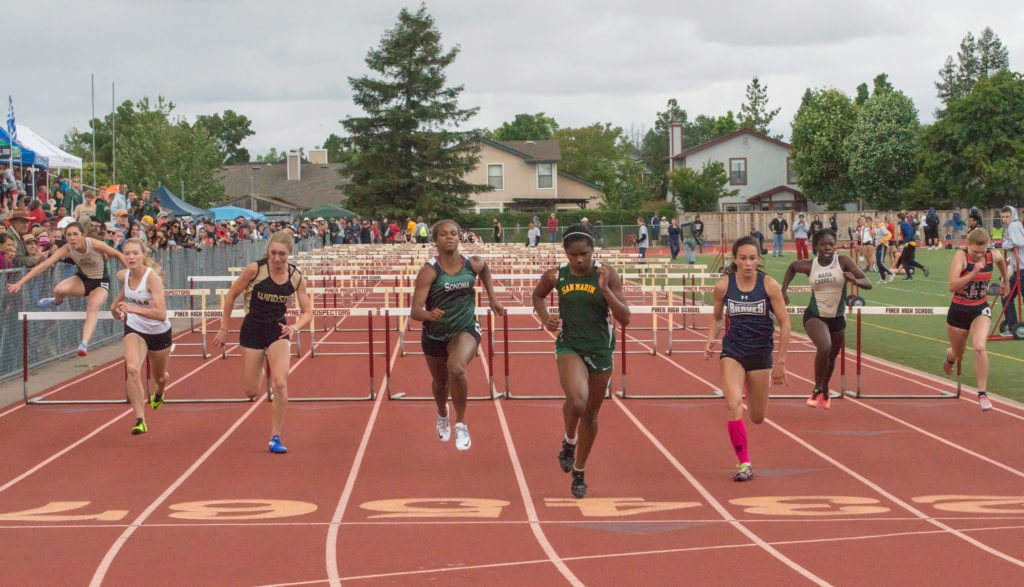 Athlete prepares for pole vault on a track with others watching.