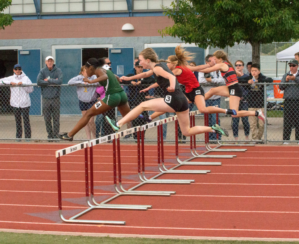 Athlete prepares for pole vault on a track with others watching.