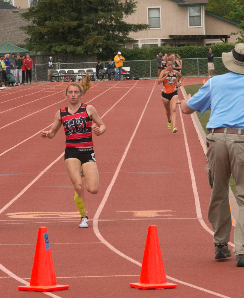 Athlete prepares for pole vault on a track with others watching.