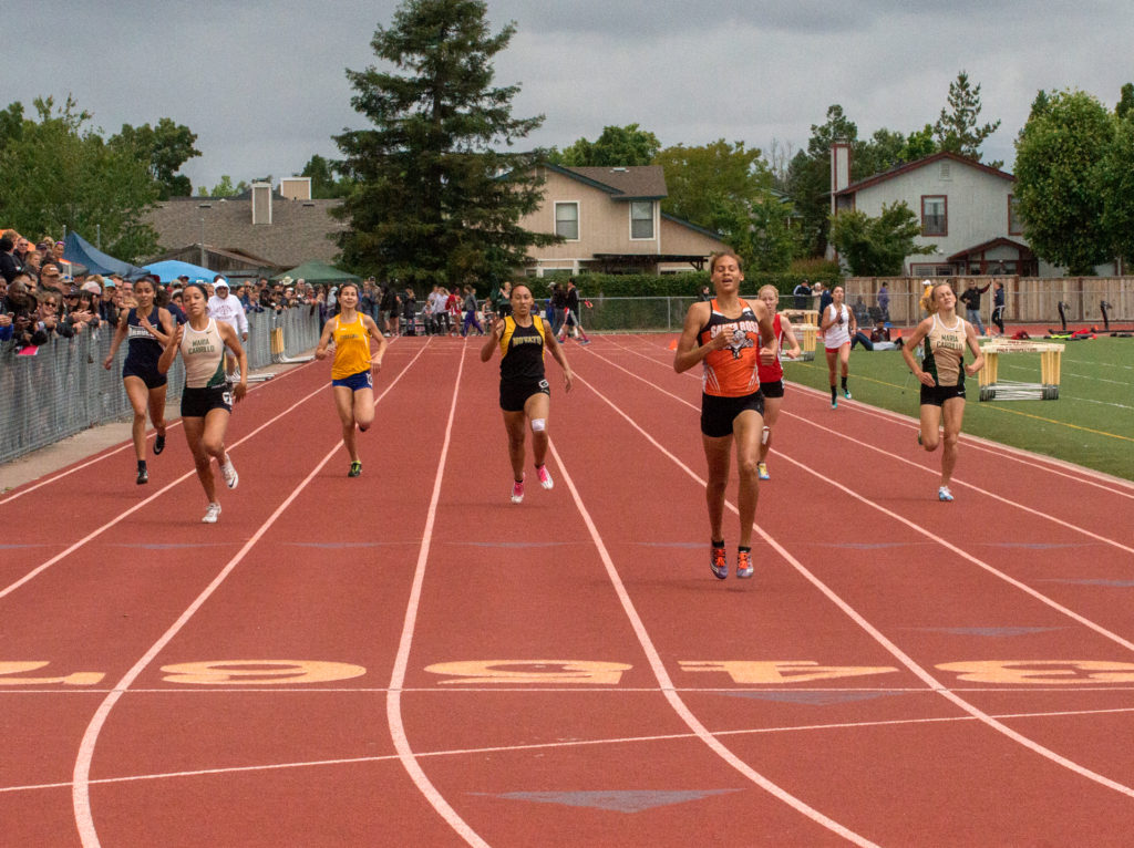 Athlete prepares for pole vault on a track with others watching.
