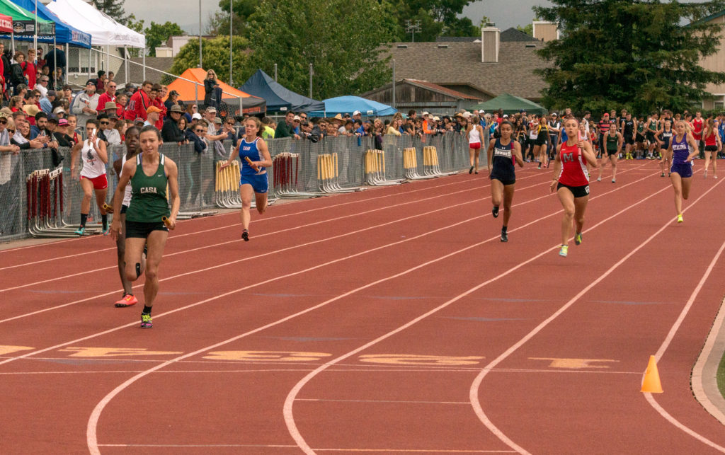 Athlete prepares for pole vault on a track with others watching.