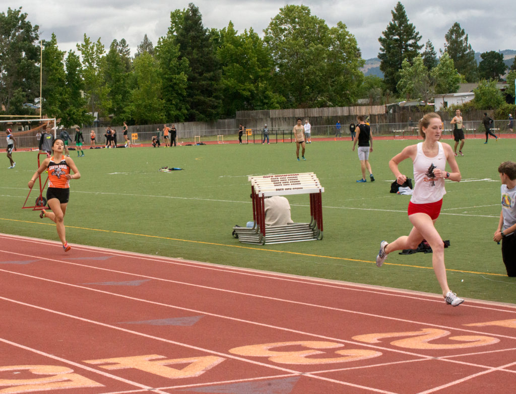 Athlete prepares for pole vault on a track with others watching.