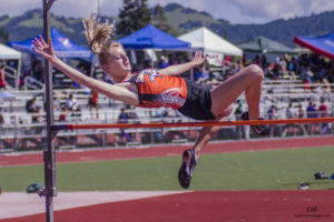 Athlete prepares for pole vault on a track with others watching.