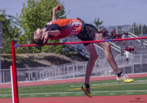 Athlete prepares for pole vault on a track with others watching.
