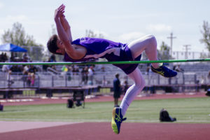 Athlete prepares for pole vault on a track with others watching.