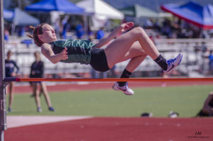 Athlete prepares for pole vault on a track with others watching.
