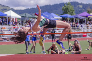 Athlete prepares for pole vault on a track with others watching.
