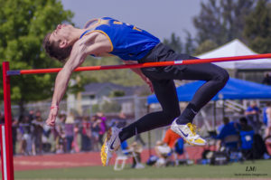 Athlete prepares for pole vault on a track with others watching.