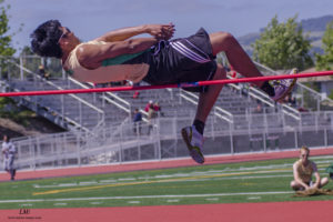 Athlete prepares for pole vault on a track with others watching.