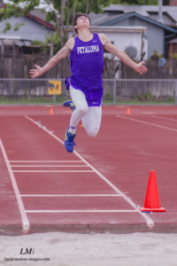 Athlete prepares for pole vault on a track with others watching.