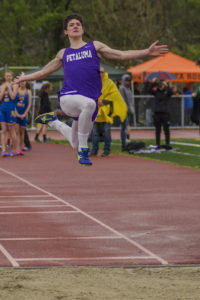 Athlete prepares for pole vault on a track with others watching.