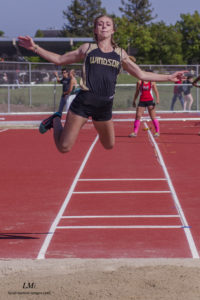 Athlete prepares for pole vault on a track with others watching.