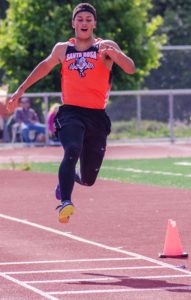 Athlete prepares for pole vault on a track with others watching.