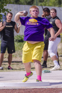 Athlete prepares for pole vault on a track with others watching.