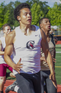 Athlete prepares for pole vault on a track with others watching.
