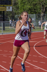 Athlete prepares for pole vault on a track with others watching.