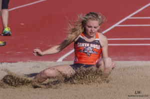 Athlete prepares for pole vault on a track with others watching.