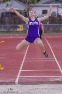 Athlete prepares for pole vault on a track with others watching.