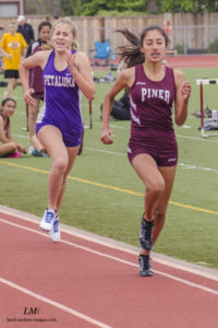 Athlete prepares for pole vault on a track with others watching.
