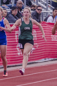 Athlete prepares for pole vault on a track with others watching.