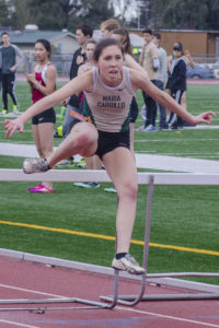 Athlete prepares for pole vault on a track with others watching.