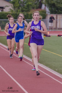 Athlete prepares for pole vault on a track with others watching.
