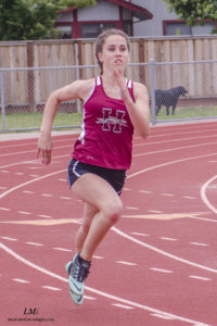 Athlete prepares for pole vault on a track with others watching.