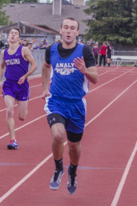 Athlete prepares for pole vault on a track with others watching.