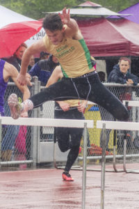Athlete prepares for pole vault on a track with others watching.