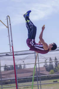 Athlete prepares for pole vault on a track with others watching.