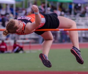 Athlete prepares for pole vault on a track with others watching.