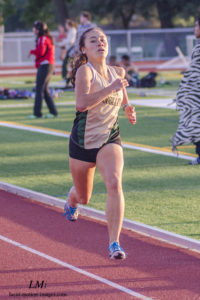 Athlete prepares for pole vault on a track with others watching.