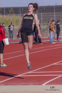 Athlete prepares for pole vault on a track with others watching.