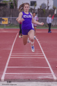 Athlete prepares for pole vault on a track with others watching.