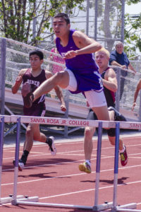 Athlete prepares for pole vault on a track with others watching.