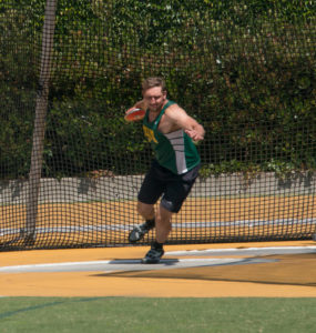 Athlete prepares for pole vault on a track with others watching.